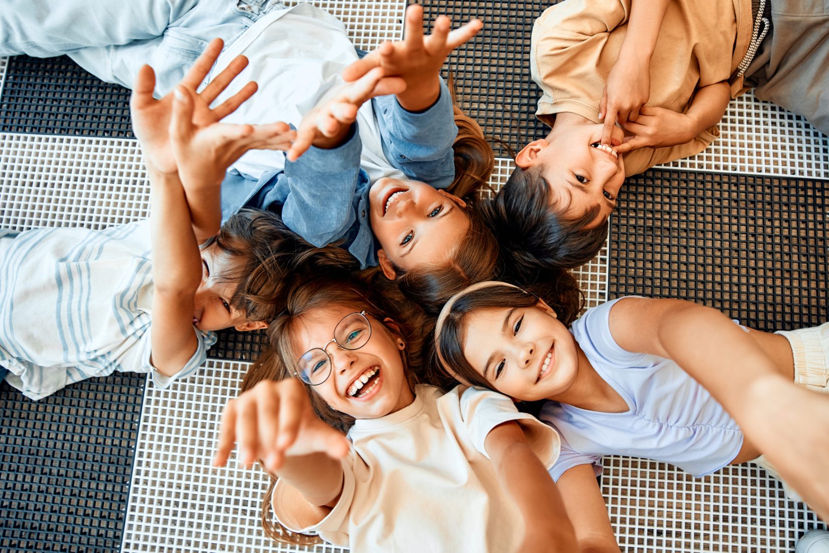 Back to school. Cheerful schoolchildren lying on the floor and smiling at the camera, top view. Education and science concept.